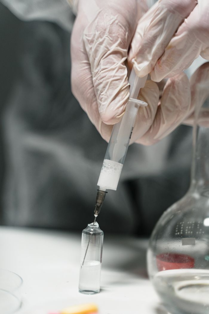 who-we-are Close-up of hands in gloves using a syringe to extract liquid from a vial in a lab setting.